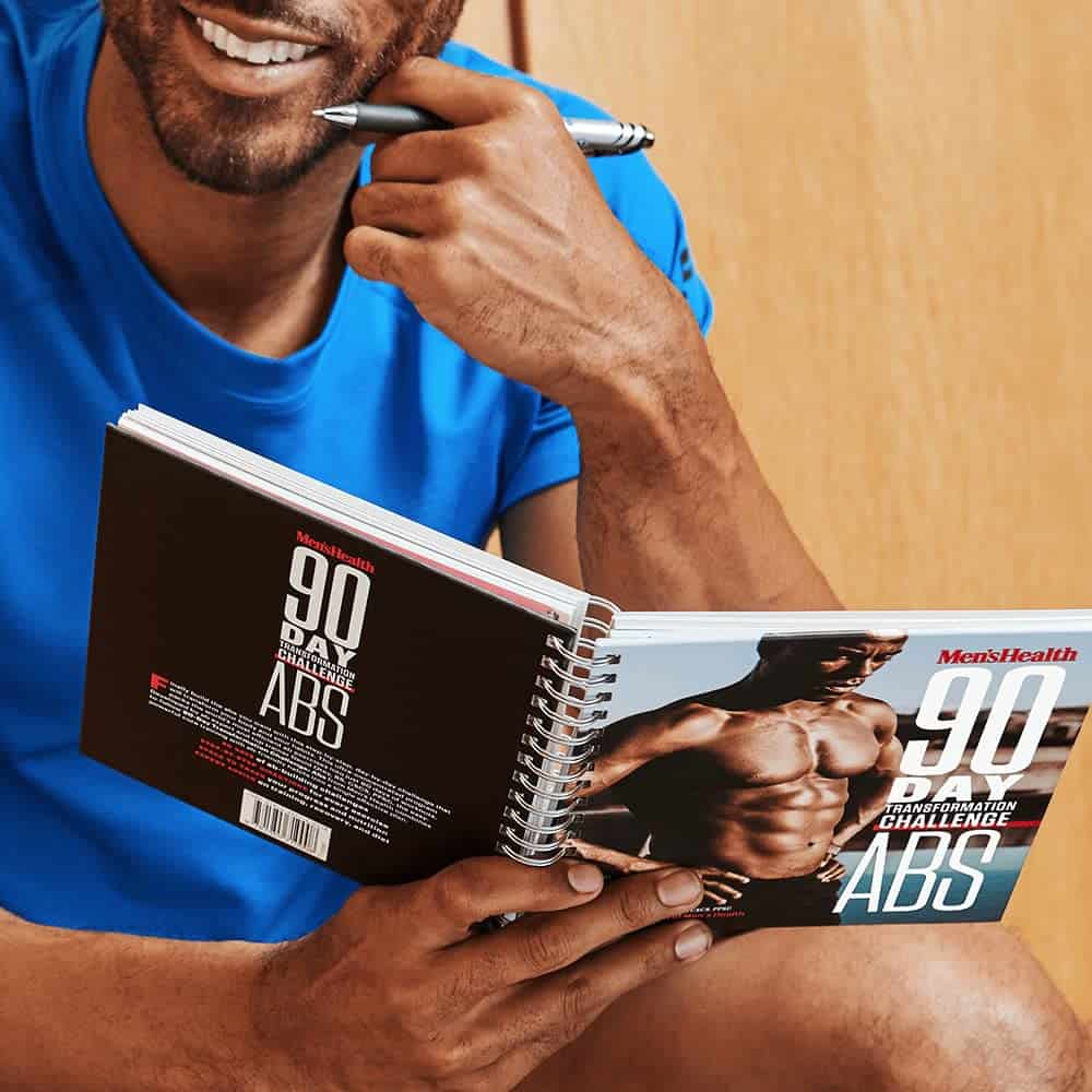 Man holding a '90 Day Ab Challenge' book with a pen, wearing a blue shirt.