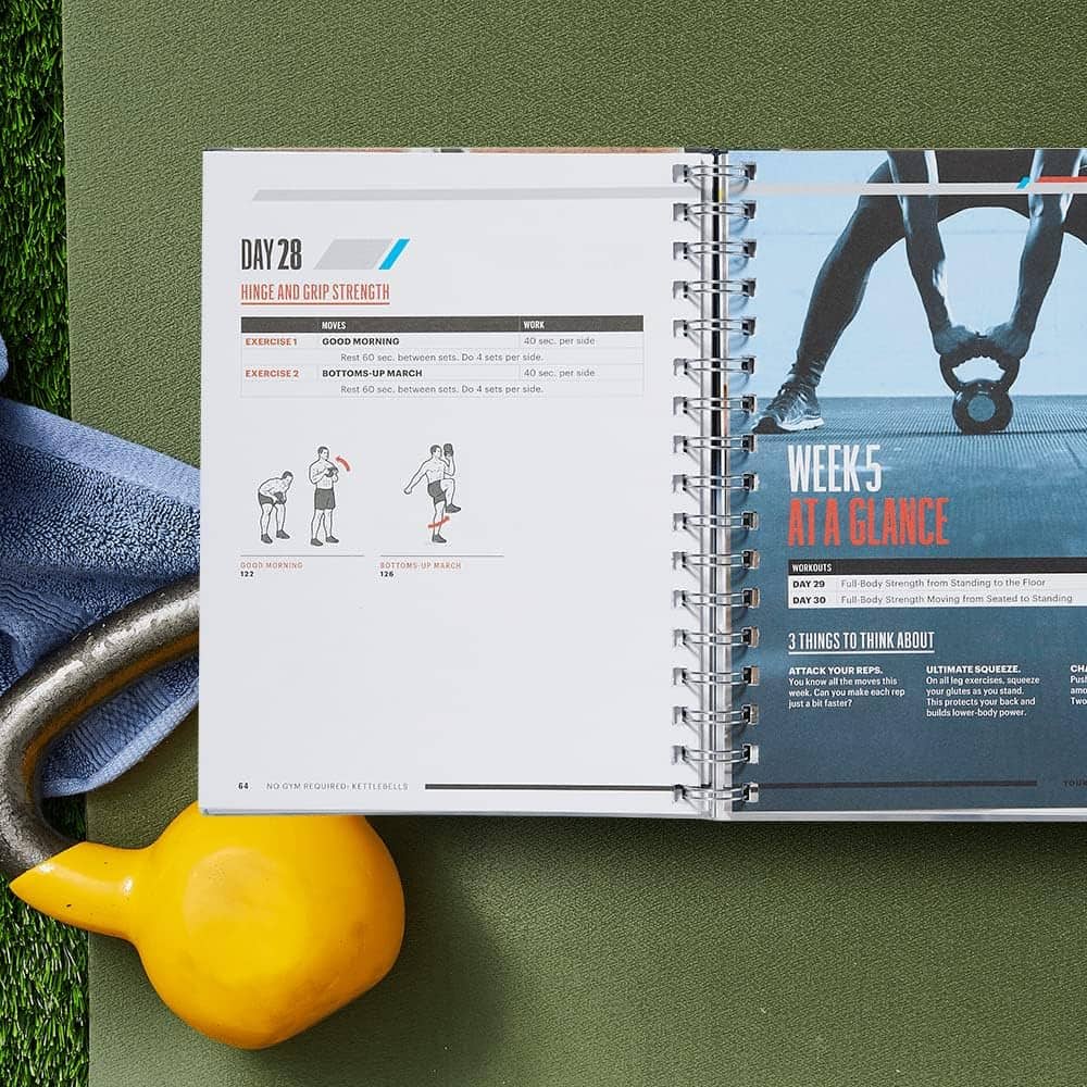 Open fitness planner with workout pages on a green surface with gym equipment.