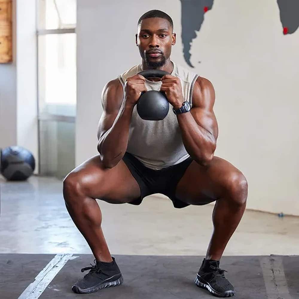Man performing a squat exercise with a kettlebell in a gym setting