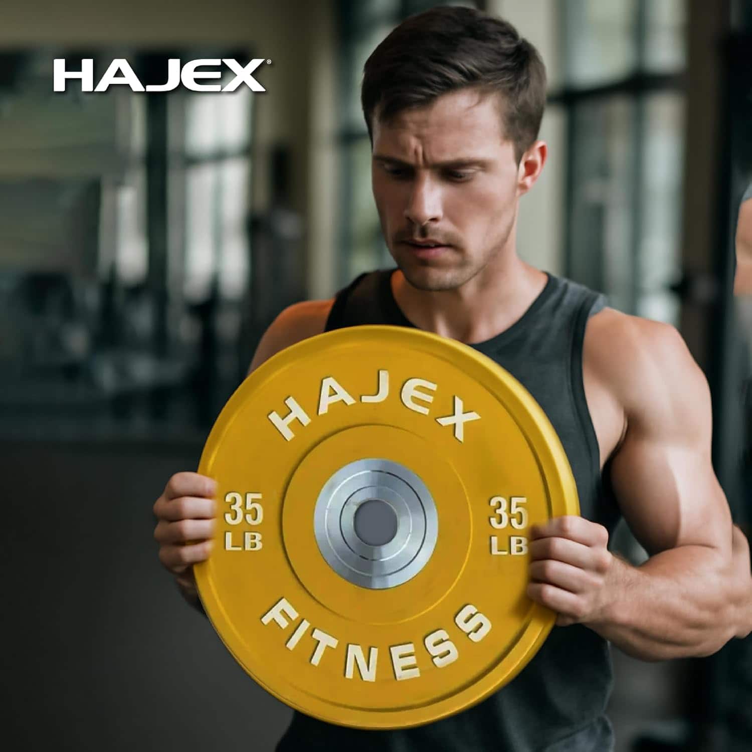 Man holding a yellow Hajex fitness weight plate in a gym setting