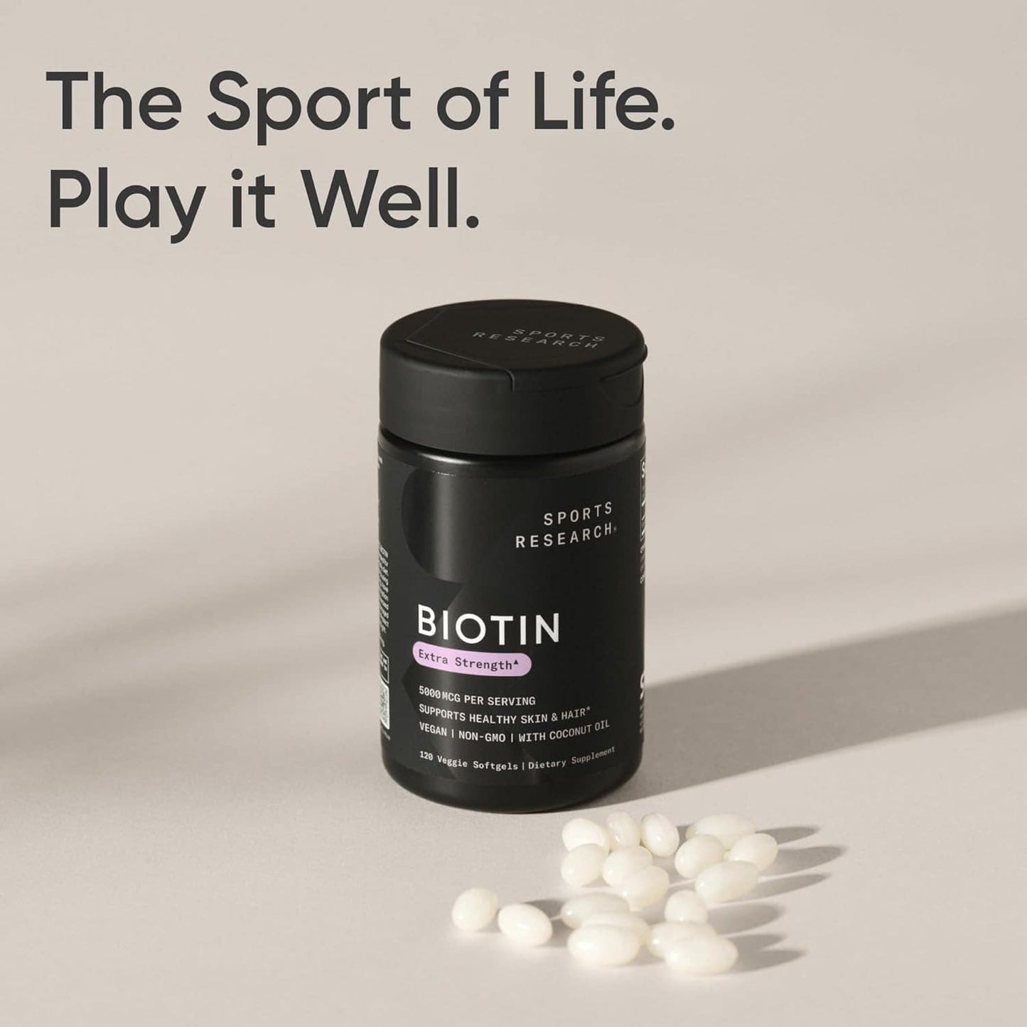 Biotin supplement bottle with scattered capsules on a neutral background, featuring the text 'The Sport of Life. Play it Well.