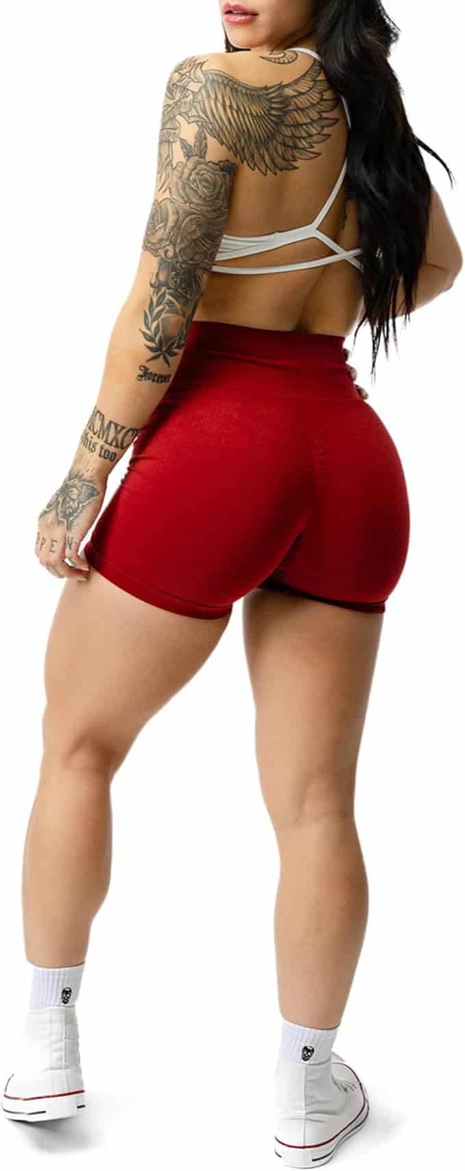 Person wearing red shorts and a white crop top with tattoos on arms and back.