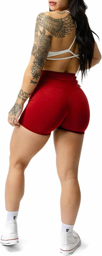 Person wearing red shorts and a white crop top with tattoos on arms and back.