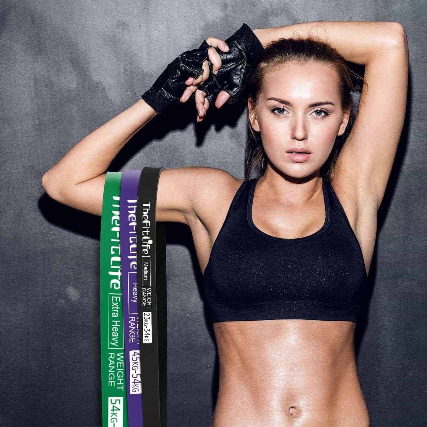 Woman in black sports bra and gloves with weightlifting straps on a gray background