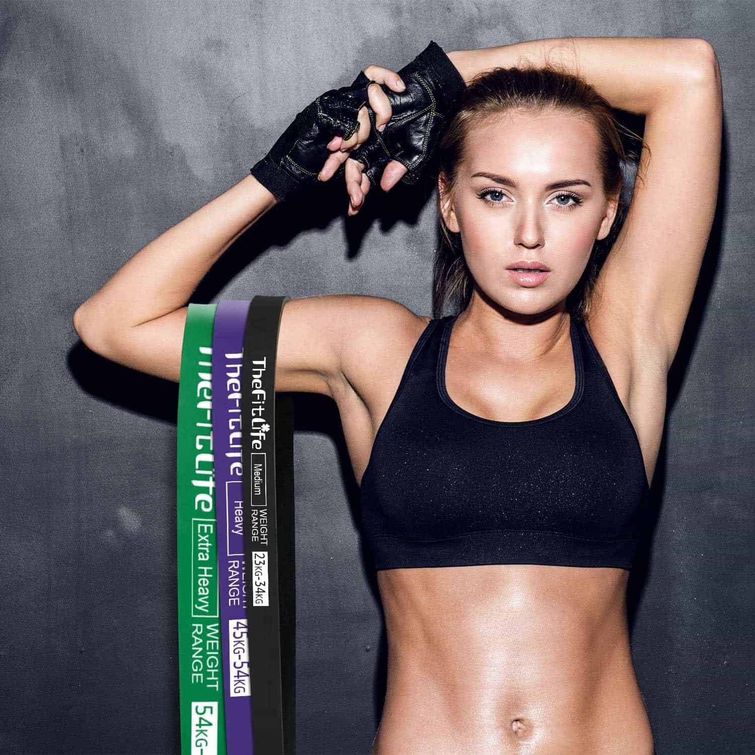 Woman in black sports bra and gloves with weightlifting straps on a gray background