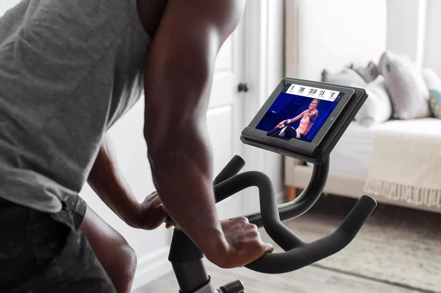 Person using a stationary bike with a tablet displaying a workout video in a home setting.